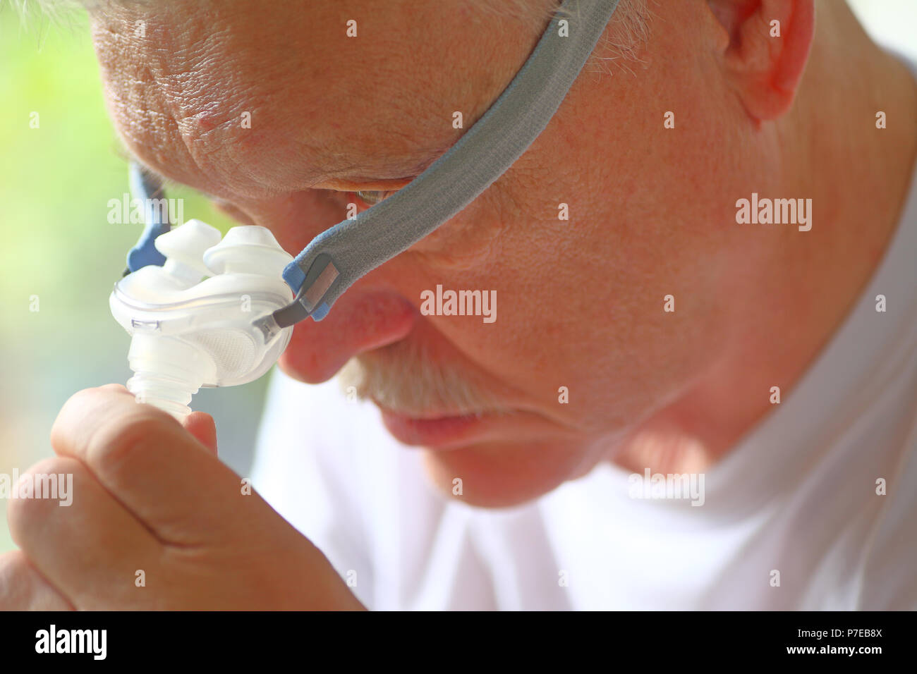 Älterer Mann passt den Nasenbügel und Kopfbedeckungen Teil seiner Behandlung von Schlafapnoe Gerät Stockfoto