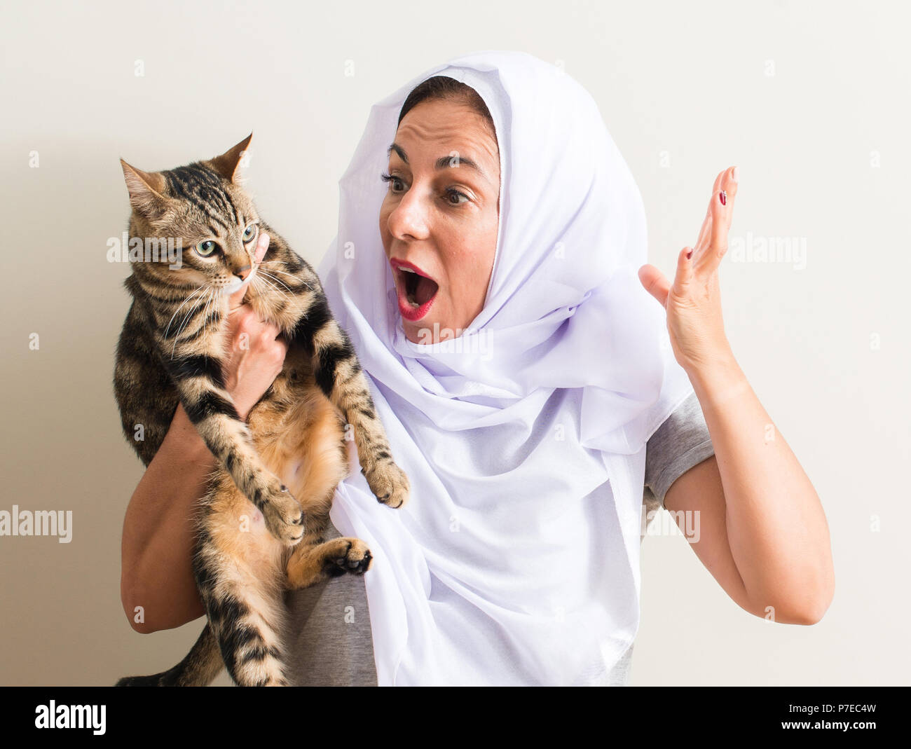 1001 Frau tragen weiße hijab Halten einer Katze sehr glücklich und aufgeregt, Sieger Ausdruck feiern Sieg schreien mit Lächeln und hob die Hand Stockfoto