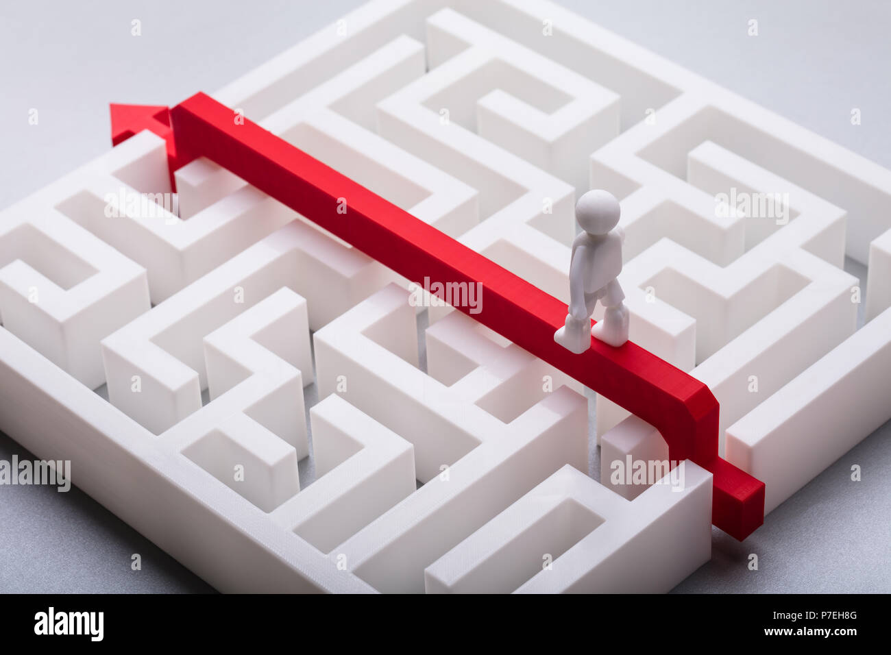 Nahaufnahme der menschlichen Figur Kreuzung weißen Labyrinth über den roten Pfeil Stockfoto