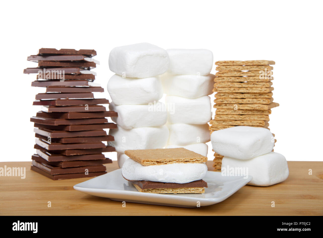 Hausgemachte s'More auf eine quadratische Platte mit Stapeln von graham Cracker, Schokolade und Marshmallows auf einem Holztisch, isoliert auf weißem Hintergrund. Stockfoto