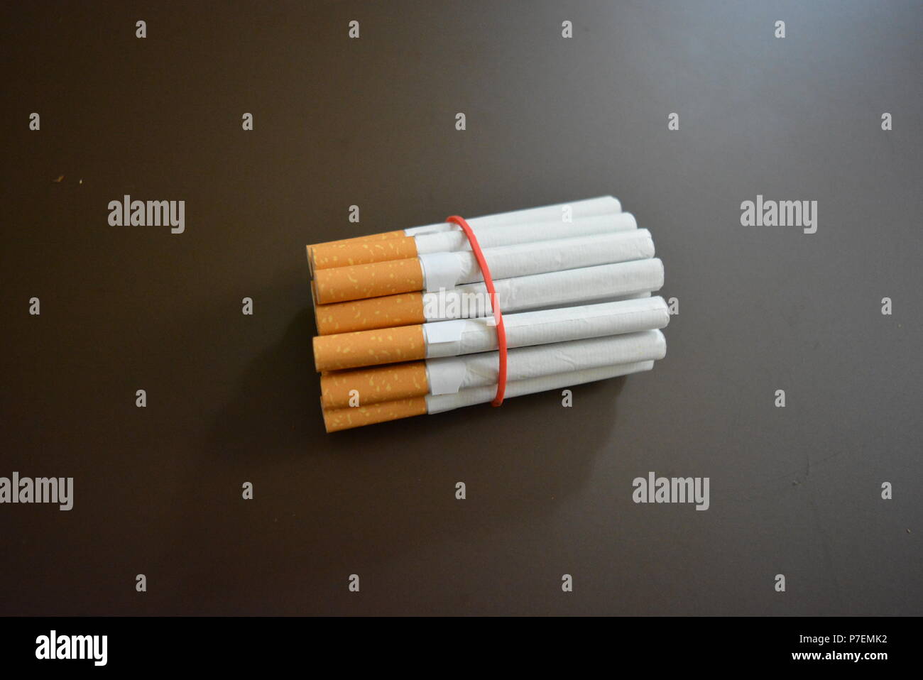 Zigaretten aus der Packung sind mit einem roten Gummi auf einem Braunen matten Hintergrund fixiert. Stockfoto