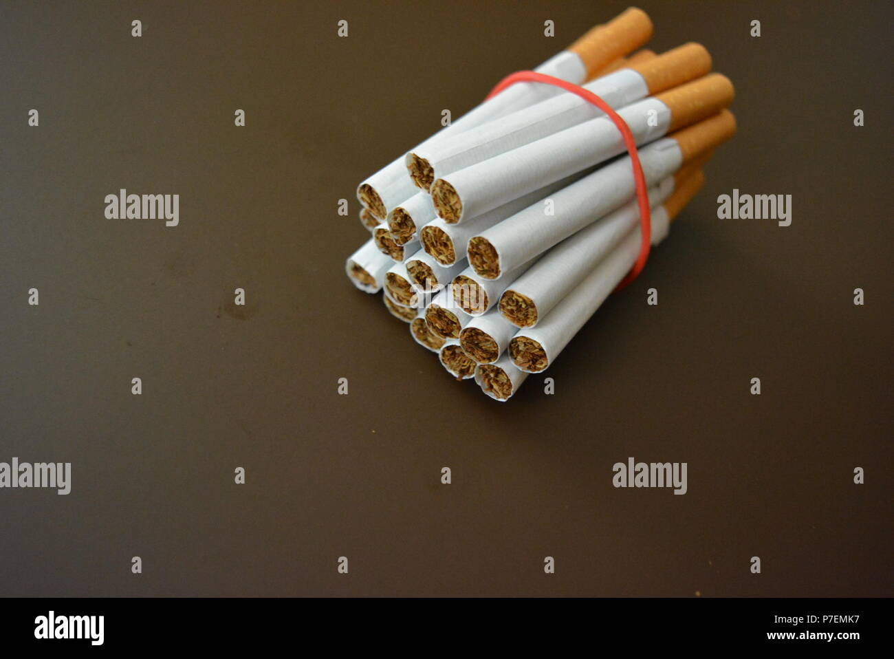 Zigaretten aus der Packung sind mit einem roten Gummi auf einem Braunen matten Hintergrund fixiert. Stockfoto