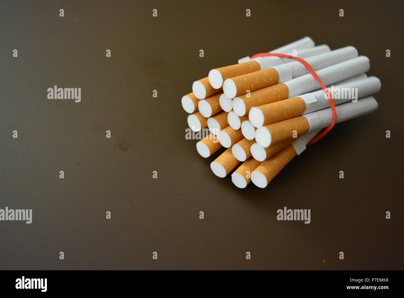 Zigaretten aus der Packung sind mit einem roten Gummi auf einem Braunen matten Hintergrund fixiert. Stockfoto