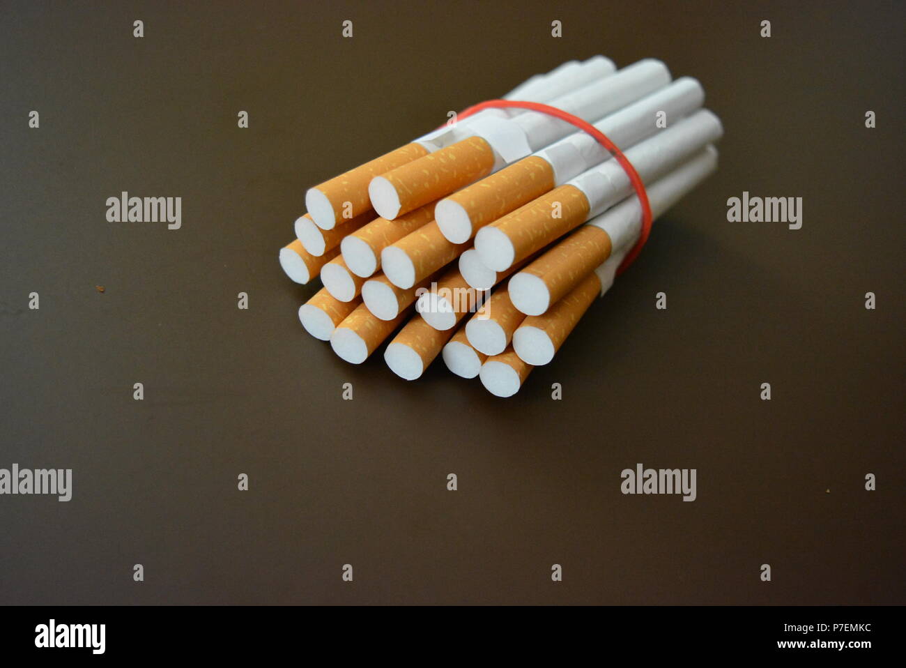 Zigaretten aus der Packung sind mit einem roten Gummi auf einem Braunen matten Hintergrund fixiert. Stockfoto