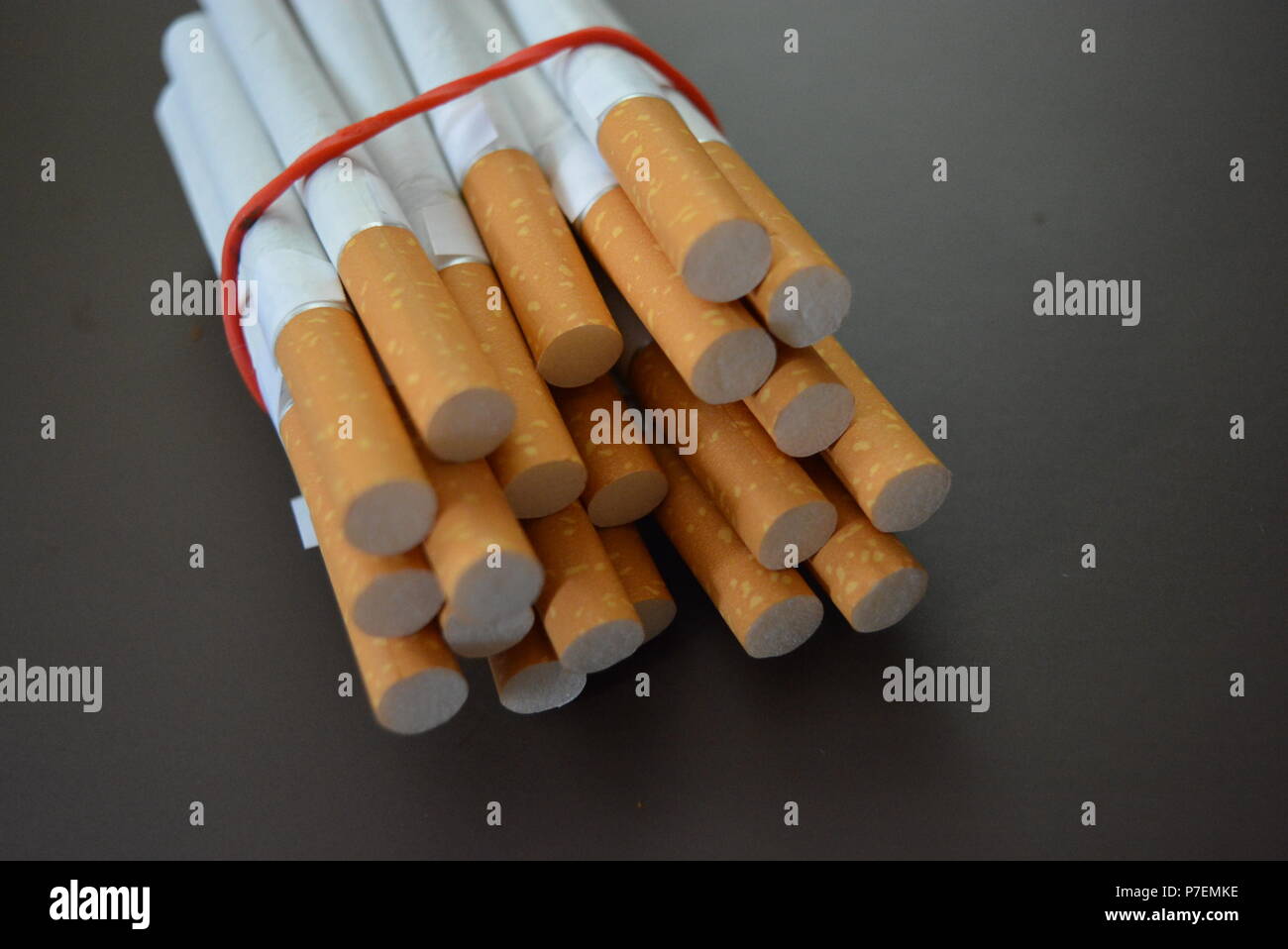 Zigaretten aus der Packung sind mit einem roten Gummi auf einem Braunen matten Hintergrund fixiert. Stockfoto