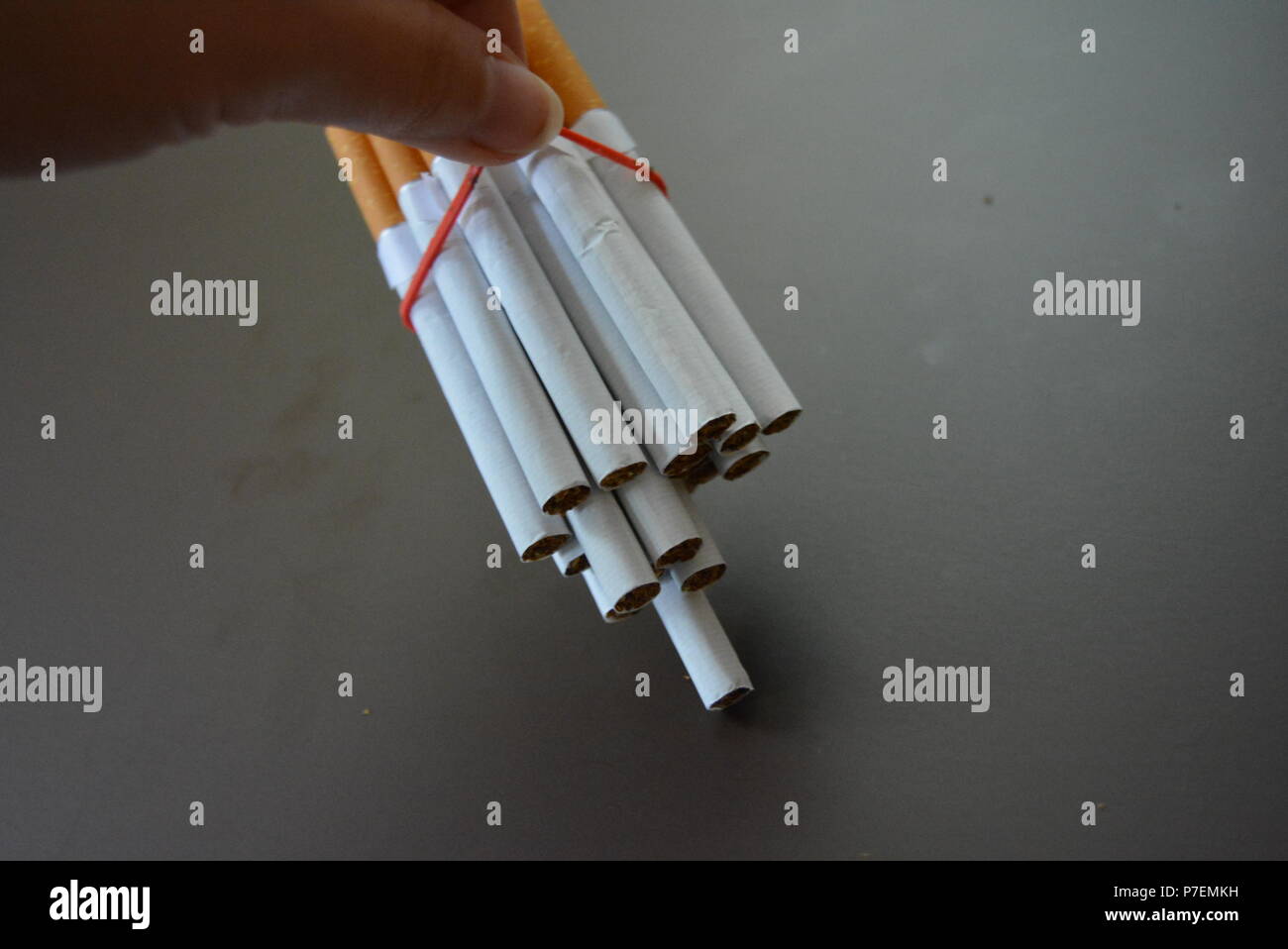 Zigaretten aus der Packung sind mit einem roten Gummi auf einem Braunen matten Hintergrund fixiert. Stockfoto