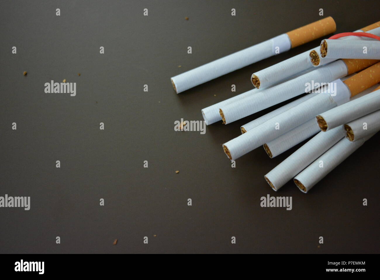 Zigaretten aus der Packung sind mit einem roten Gummi auf einem Braunen matten Hintergrund fixiert. Stockfoto