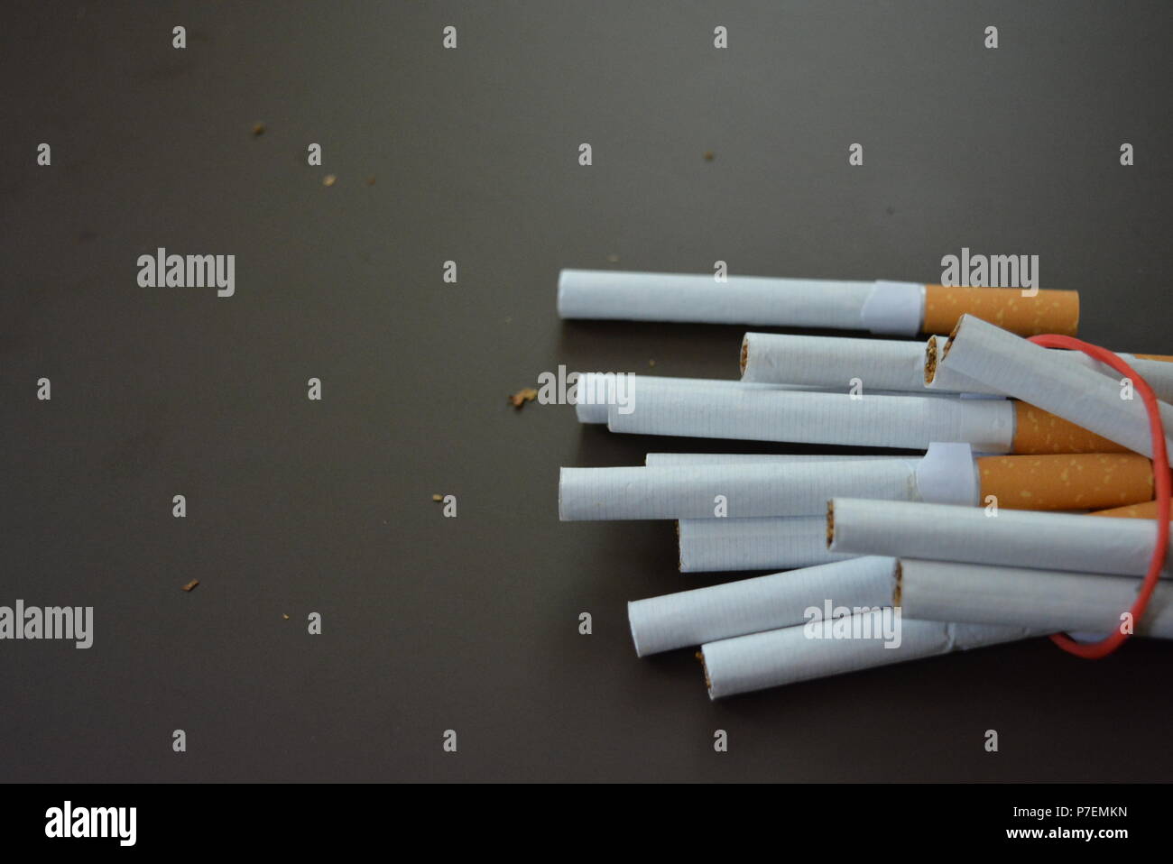 Zigaretten aus der Packung sind mit einem roten Gummi auf einem Braunen matten Hintergrund fixiert. Stockfoto