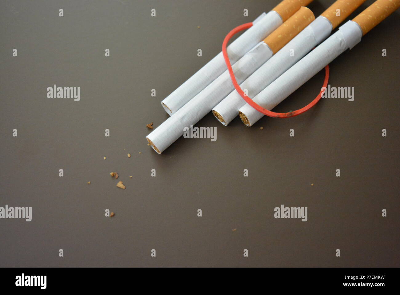 Zigaretten aus der Packung sind mit einem roten Gummi auf einem Braunen matten Hintergrund fixiert. Stockfoto