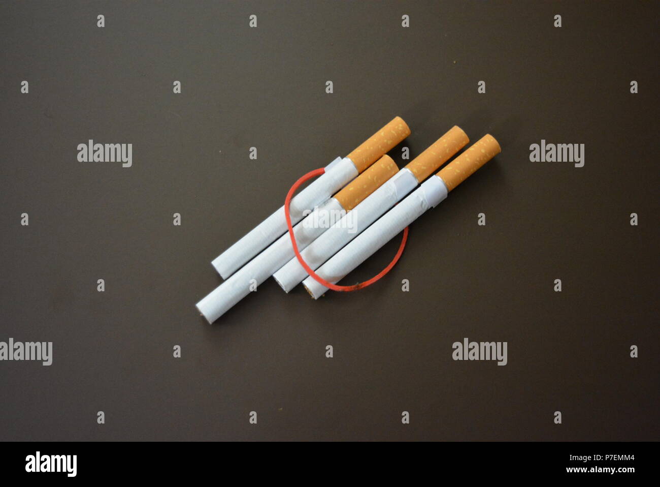 Zigaretten aus der Packung sind mit einem roten Gummi auf einem Braunen matten Hintergrund fixiert. Stockfoto