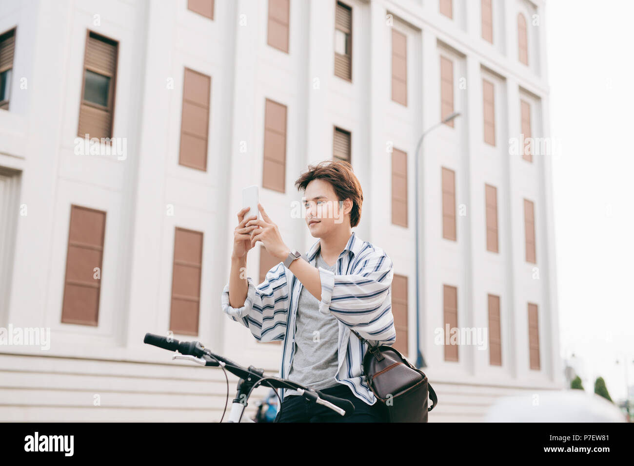 Stilvolle Menschen chatten, während Sie Handy beim Sitzen auf dem Fahrrad, im Freien. Im karierten Hemd, T-Shirt und Jeans. Close-up. Stockfoto