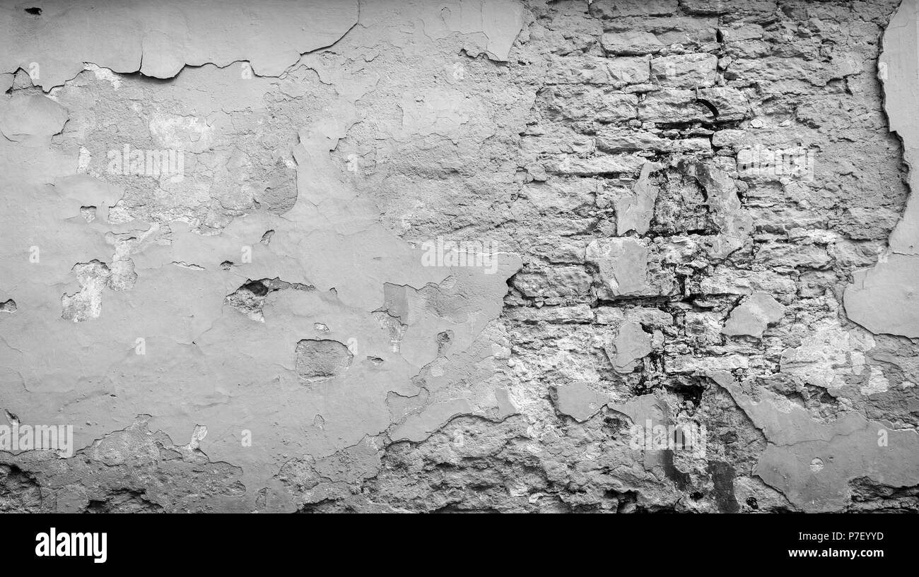 Full Frame Hintergrund einer Verwitterten, beschädigte und verputzte Wand in Schwarz und Weiß lackiert. Gips ist teilweise abgeblättert enthüllt alten Ziegelsteinen. Stockfoto