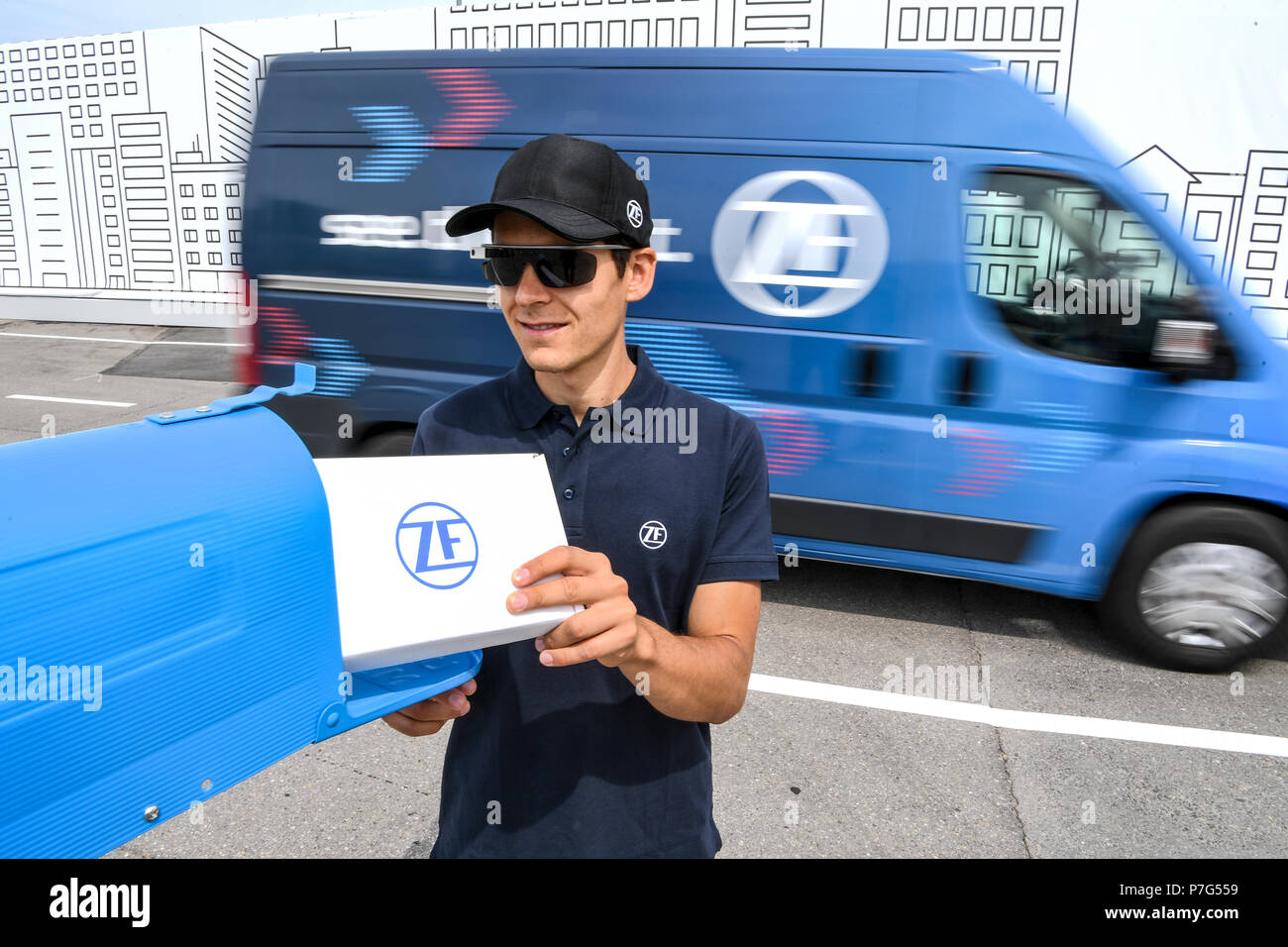 27 Juni 2018, Friedrichshafen, Deutschland: ein ZF-Mitarbeiter trägt ein Paket während der ZF-Innovation Van auf den Laufwerken selbst, zum Beispiel aus einem Nicht-parking Zone verschieben. Ein paar Daten Gläser bietet Lieferung Personal mit Informationen zu der nächsten Haltestelle. Foto: Felix Kästle/dpa Stockfoto