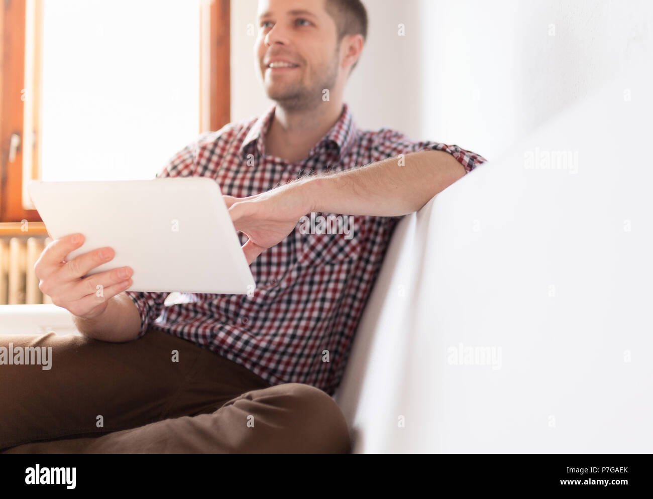 Schöner Mann auf dem Sofa zu Hause sitzen, mit einem digitalen Tablet Stockfoto