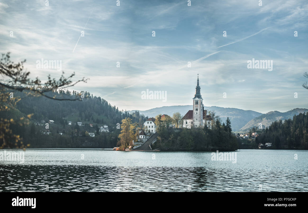 Die berühmten Bleder See Kirche mit einem warmen Glanz auf einer künstlichen Insel mit Berge und Wolken über den Himmel im Hintergrund. Stockfoto