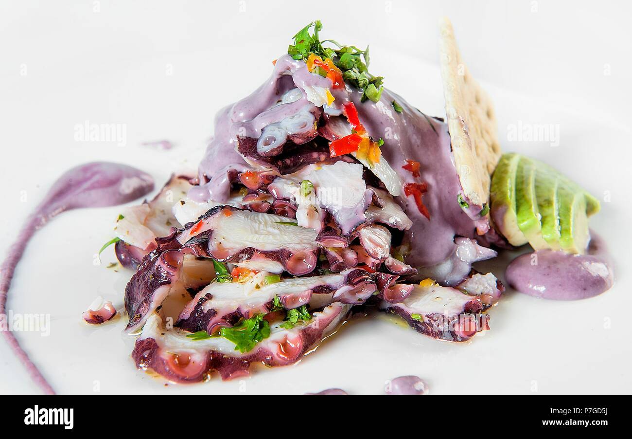 Pulpo al Olivo, traditionelles Gericht der peruanischen Küche aus einer Olive Sauce, auf einem weißen Hintergrund. Von Avocado, soda Keks- und Kopfsalat begleitet. Stockfoto