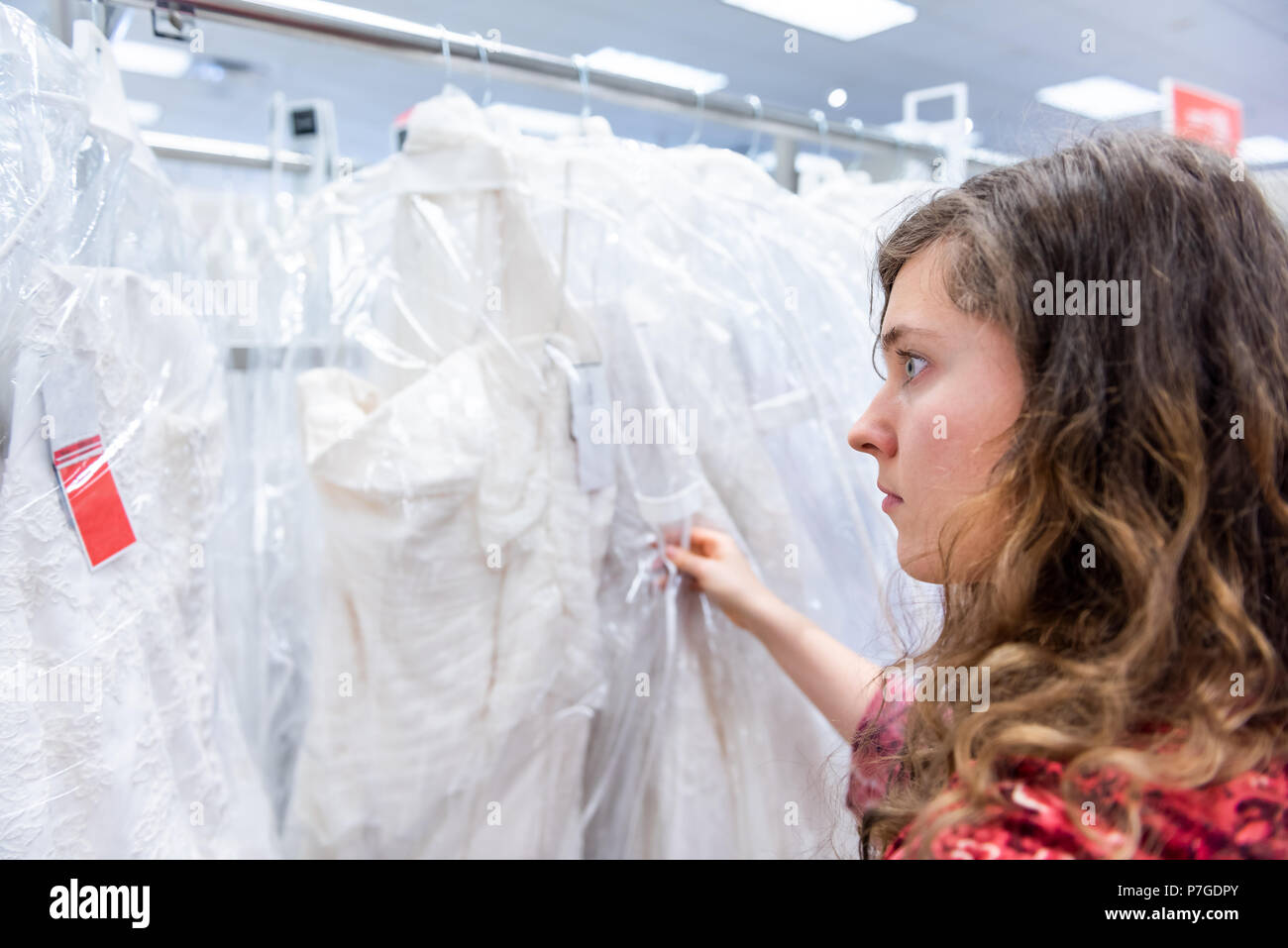 Eine junge Frau versucht, sich auf die Suche, Auswahl, berühren Brautkleider in Boutique Discounter, viele weiße Kleider hängen an Rack Kleiderbügel Zeile, Stockfoto