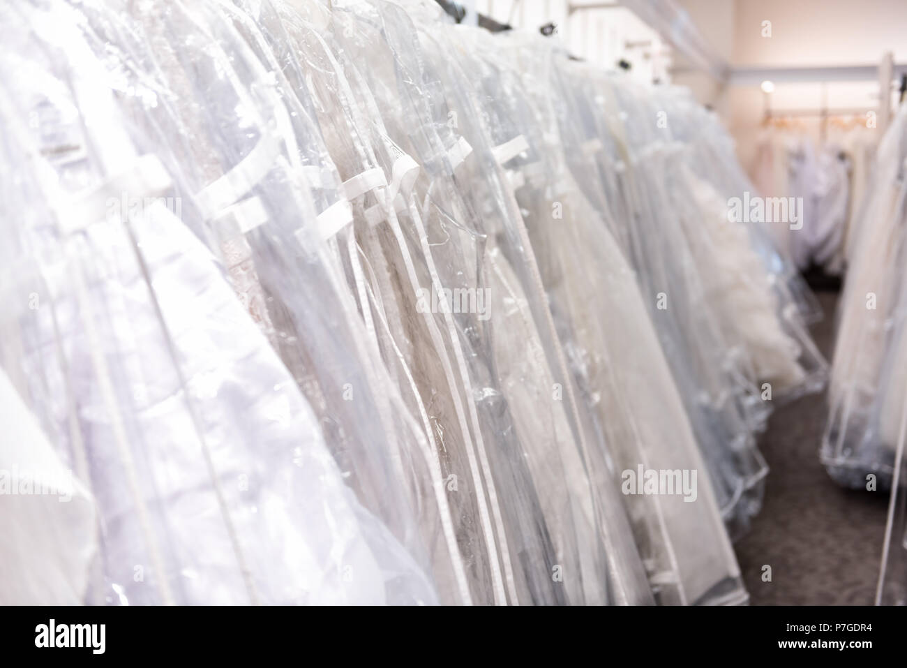 Viele Brautkleider in Boutique Diskontgeschäft, weiße Kleider hängen an Rack Kleiderbügel Reihe Nahaufnahme mit weißer Spitze, Tüll, Design Stockfoto