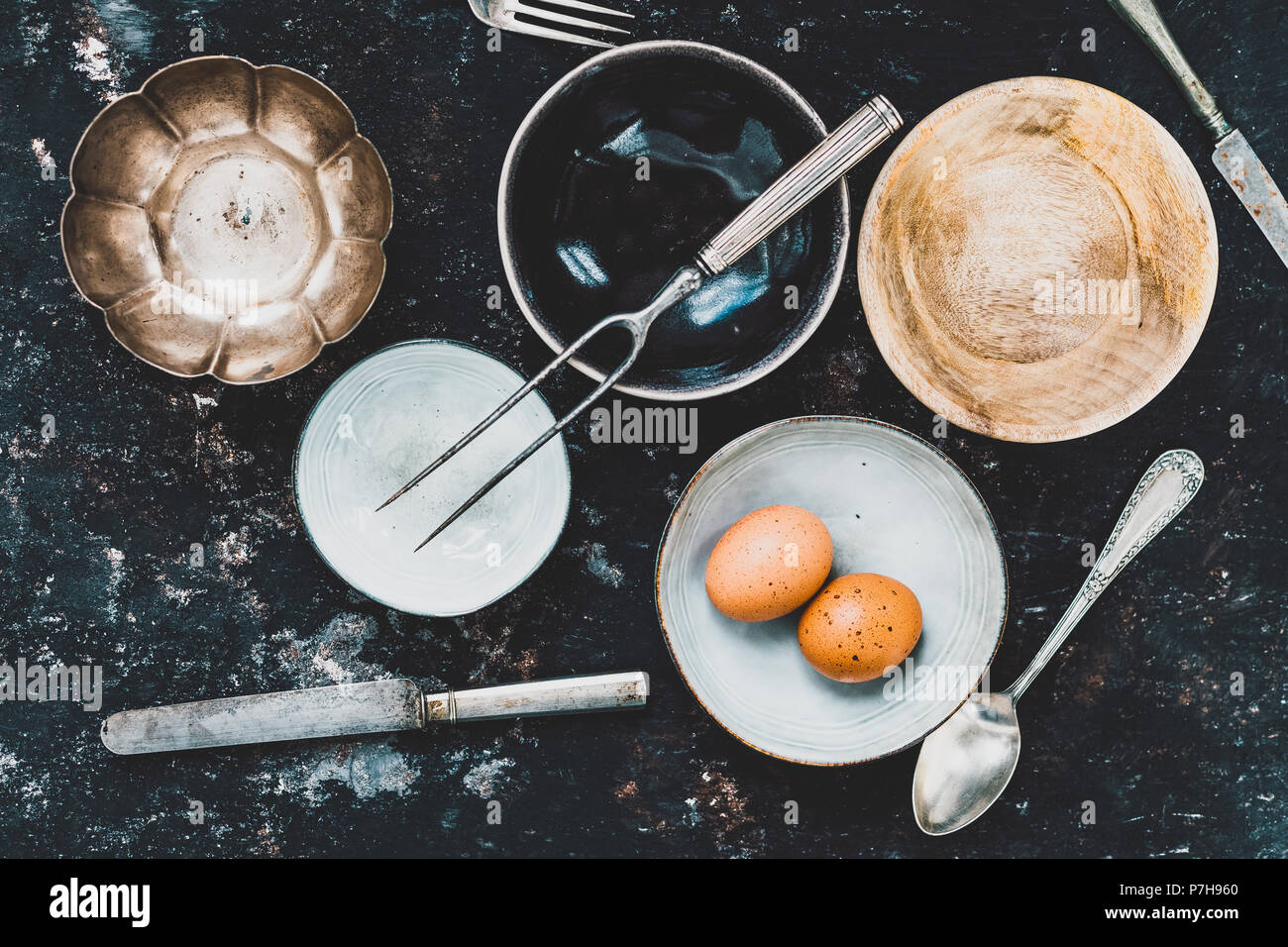 Flach mit Geschirr und Besteck aus verschiedenen Materialien auf einer rostigen dunklen Hintergrund. Foodstyling Konzept Stockfoto