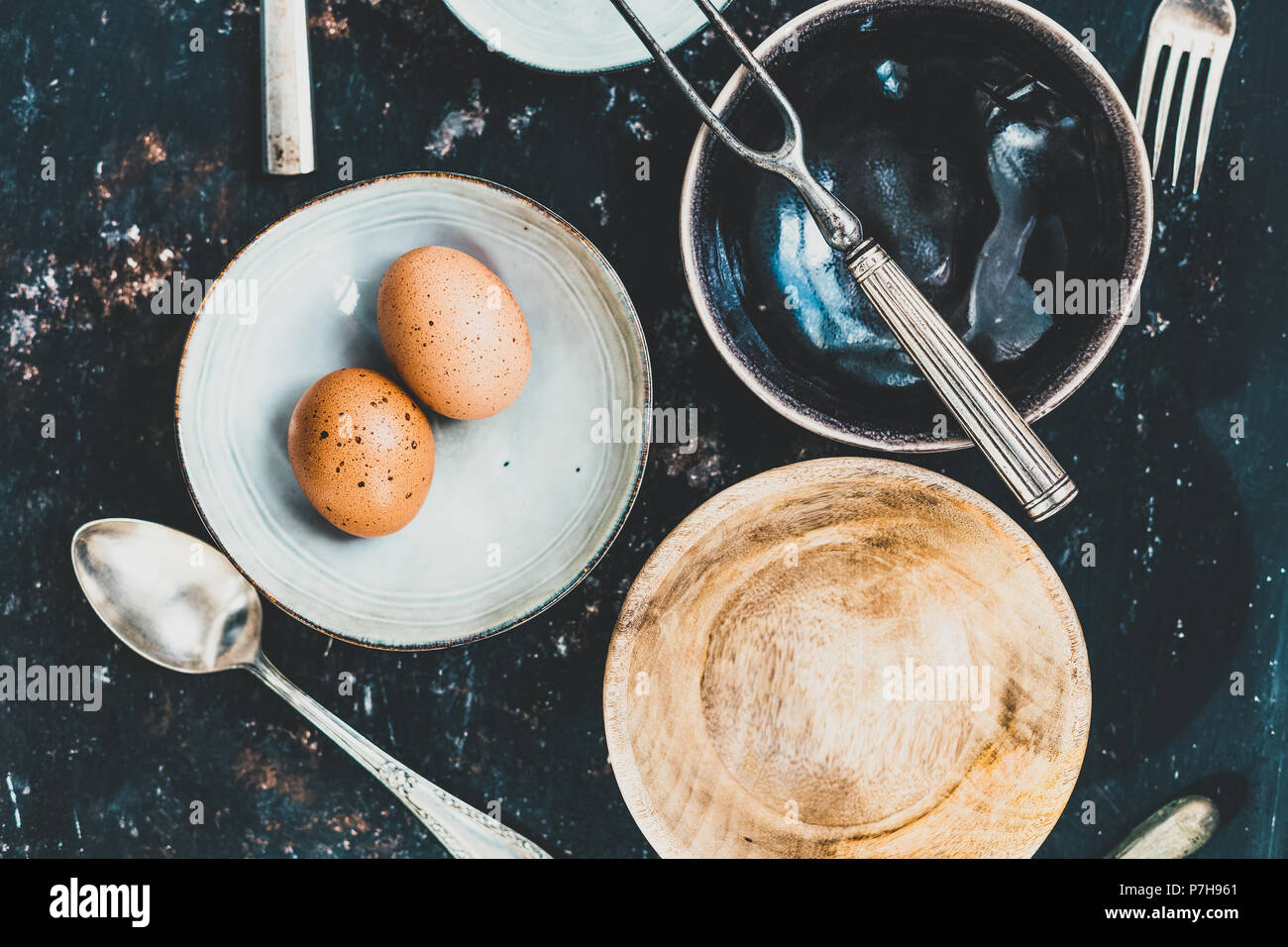 Flach mit Geschirr und Besteck aus verschiedenen Materialien auf einer rostigen dunklen Hintergrund. Foodstyling Konzept Stockfoto