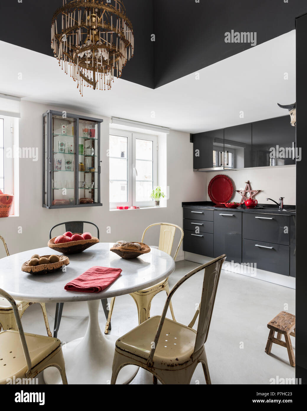 Dunkelgrau Flachbild fronted Einheiten in Küche mit Vintage metall Tolix Stühle und runde Marmorplatte Tabelle Stockfoto
