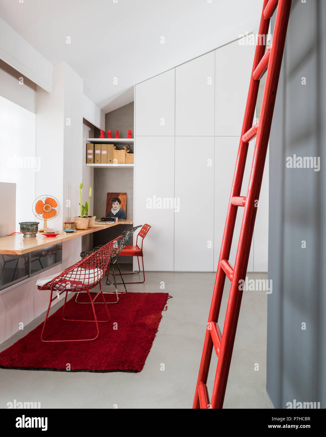 Drahtkorb Stühle an Holz Arbeitsfläche in Loft Apartment. Ein roter Leiter lehnt sich im Vordergrund. Stockfoto
