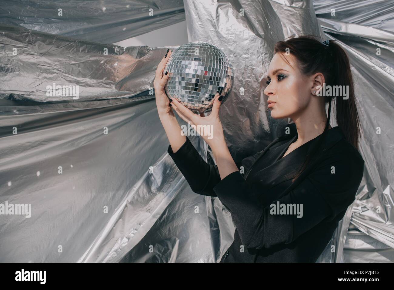 Porträt einer Frau, die in die Reflexion eines silbernen Disco ball suchen Stockfoto
