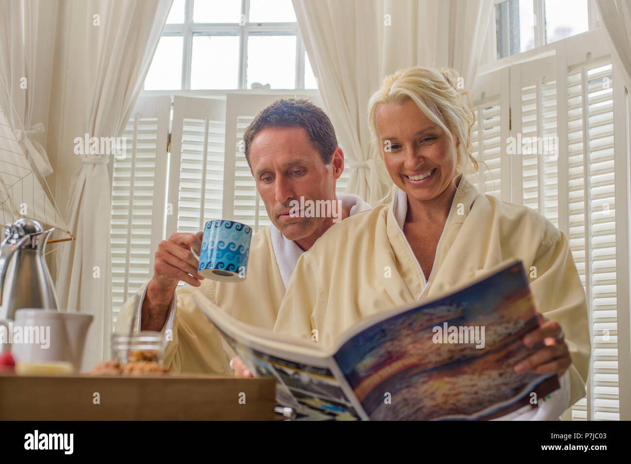 Paar in einem Hotel Zimmer eine Zeitschrift lesen und genießen das Frühstück sitzen Stockfoto