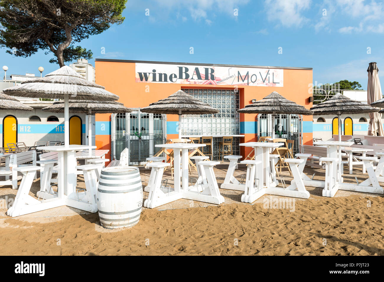 Blick auf die weißen Tischen und Sonnenschirmen vor MoVil Wein Bar, Architektur, die auf den Strand von Lignano Stockfoto