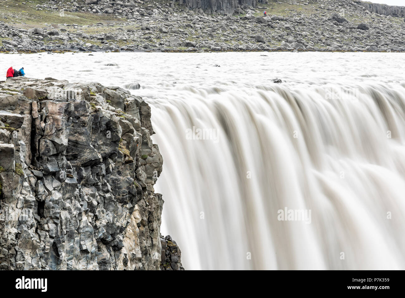 Island Wasserfall Dettifoss, der größten größten Volumen in Europa closeup, grau grau Wasser, felsigen Klippen und Menschen Touristen in Abstand, glatte lange Expo Stockfoto