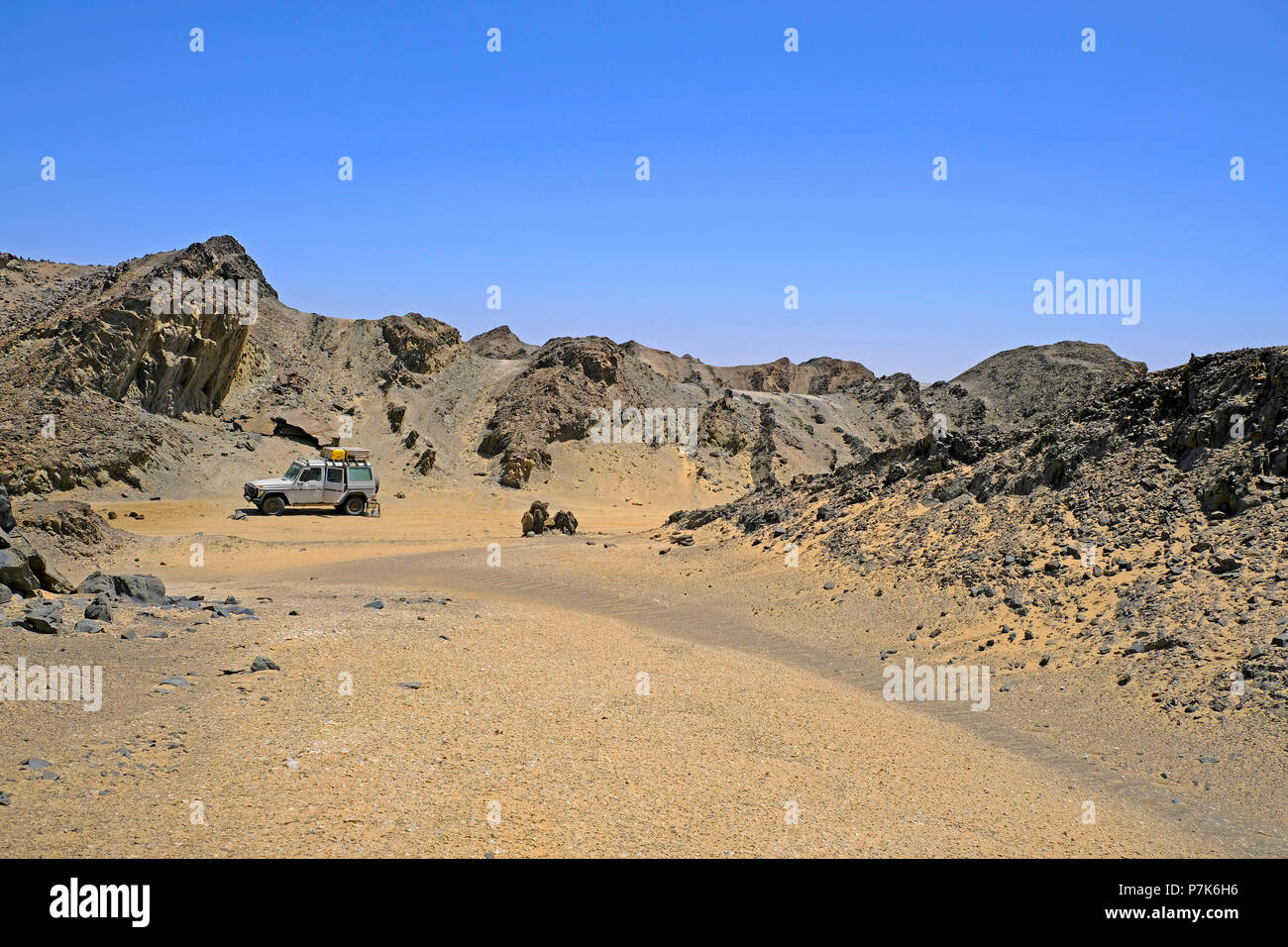 Gezackte, stark erodierte Felsformationen mit Sandanwehung und geländegängige Fahrzeuge am Kreuz - Land Flug Ugab in der Dorob Nationalpark in Namibia Stockfoto