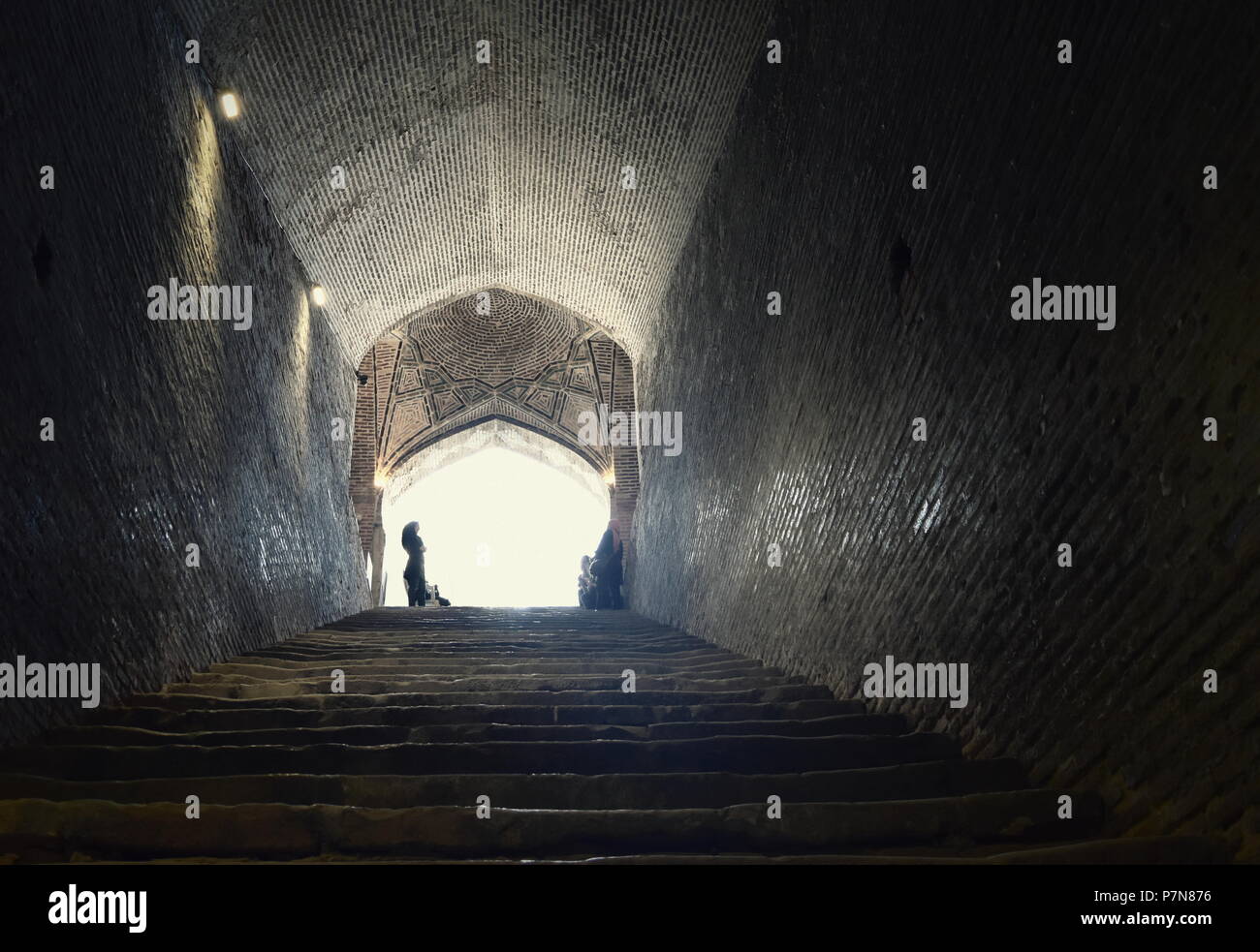Iranische muslimische Frau steht an Licht am Ende eines Tunnels und die Treppen am Eingang zu einem Silk Road U-Wasserbehälter in Qazvin, Iran Stockfoto