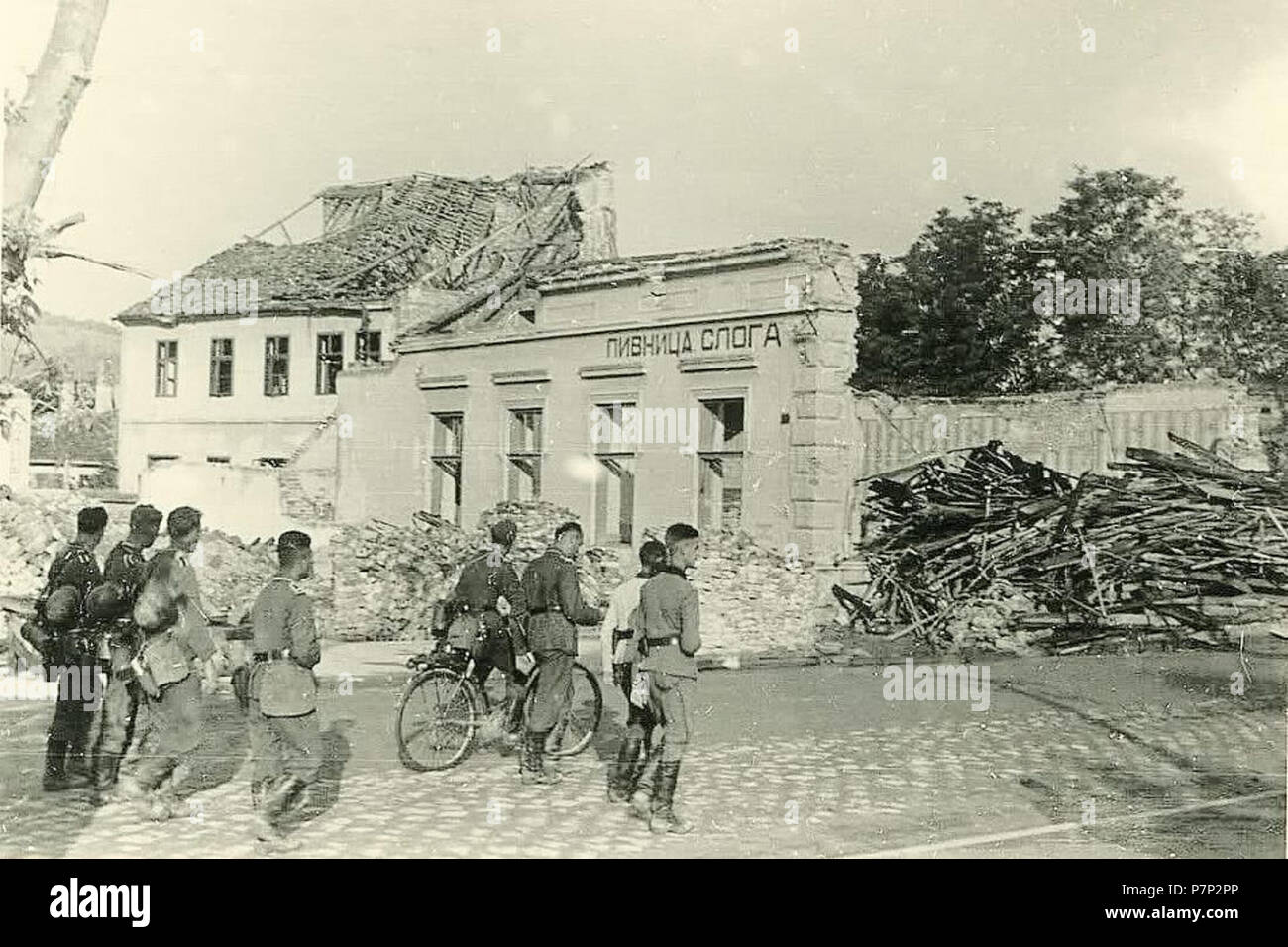 Српски / Srpski: Fotografije Smedereva neposredno Pre i nakon katastrofalne eksplozije Juna 1941. u kojoj je više poginulo hiljada ljudi u jednom Danu - Nemačka okupaciona komanda je u Grad odmah uputila trupe: vojnici prolaze offenporige prepolovljene zgrade pivnice Sloga. 1941 143 Eksplozija u Smederevu 1941 04. Stockfoto