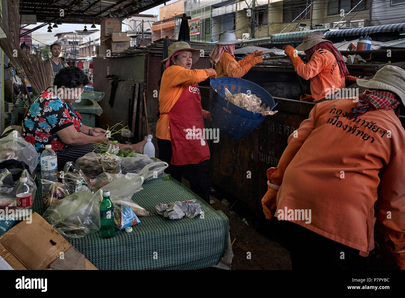 Garbage Collection mit Frau weiterhin Lebensmittel vorzubereiten trotz der Präsenz der Müllsammler beim Entleeren eines Überspringen mit Müll beladen. Thailand Stockfoto