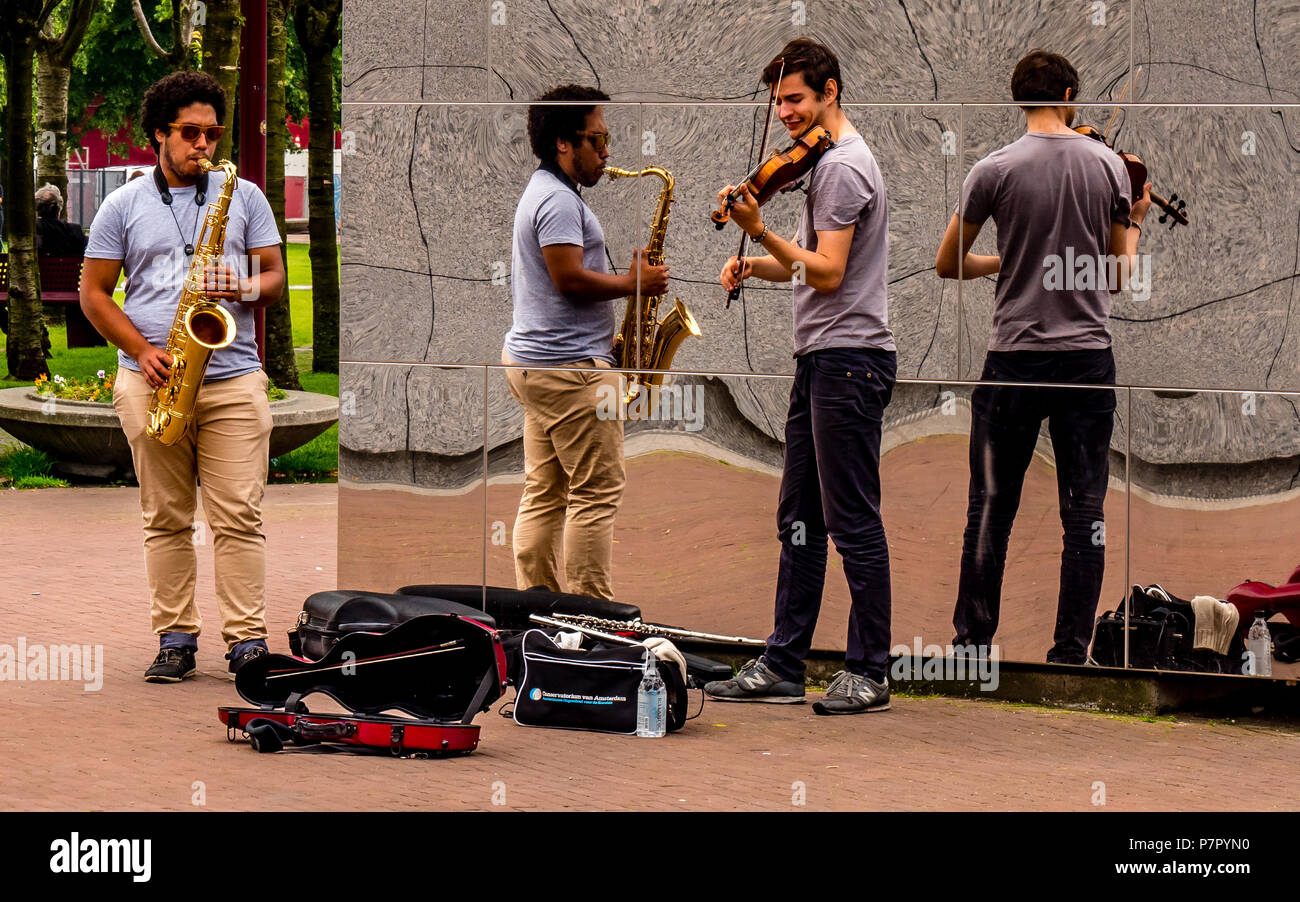 Street Performer in Amsterdam, mit Reflexion an der Wand und spielte Geige und Saxophon Musik Stockfoto