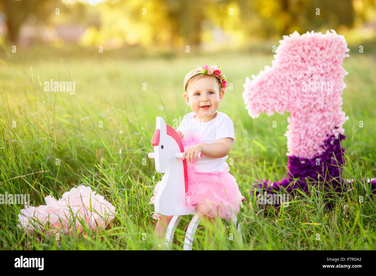 Wunderschöne kleine Mädchen in rosa Kleid reiten auf Holzspielzeug Pferd im Freien. Feier der Ersten Geburtstag Konzept Stockfoto