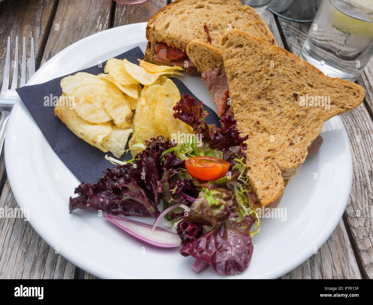 Mittagessen Snack auf einem außerhalb Café Tabelle Roastbeef Sandwich auf braunem Brot mit Salat und Kartoffelchips Stockfoto