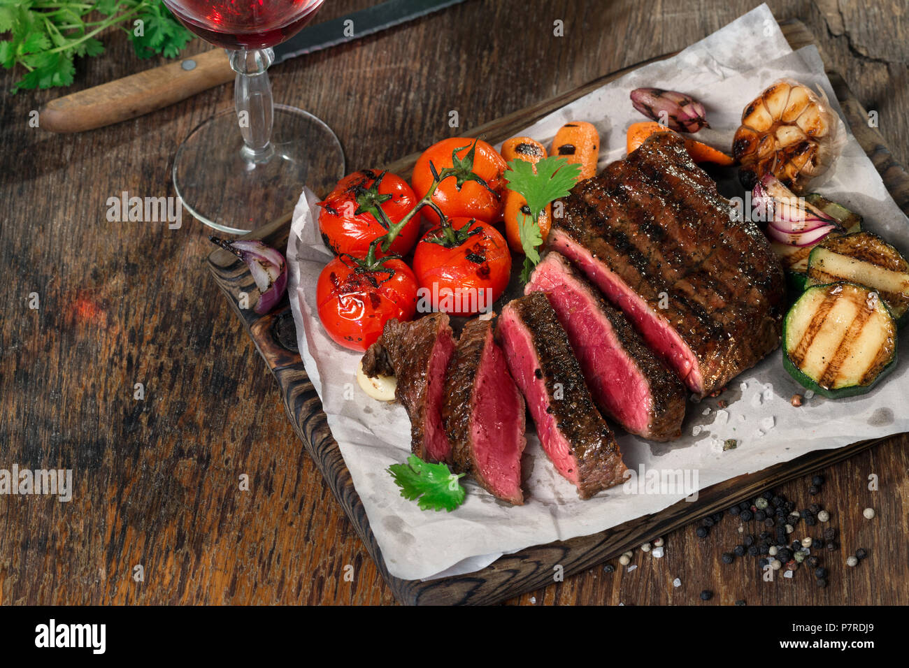 In Scheiben geschnitten Seltene gegrilltes Steak auf rustikalen Schneidbrett mit gegrilltem Gemüse auf dunklen rustikalen Tisch mit Glas Rotwein. Für text Stockfoto