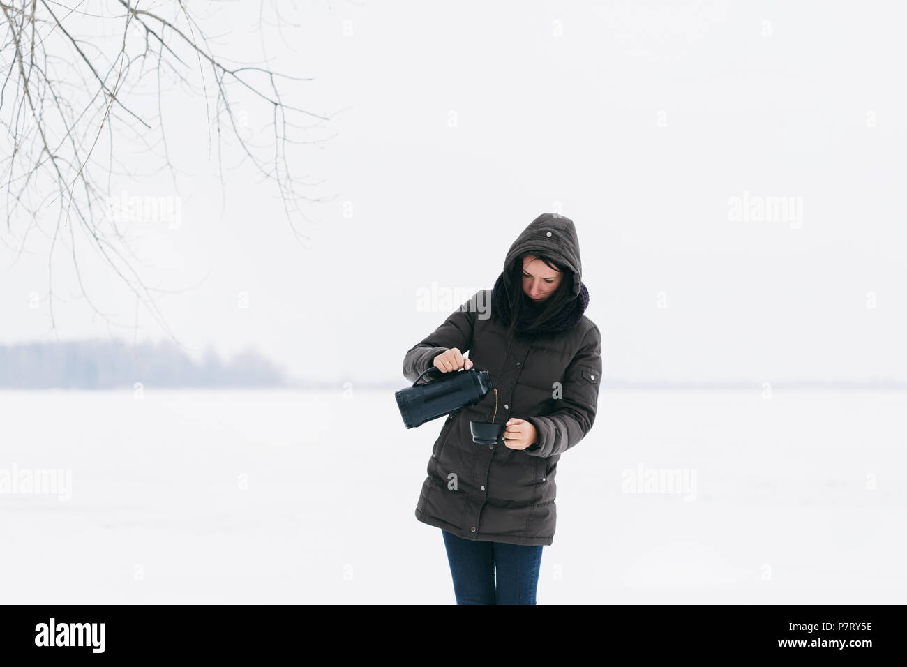 Frau im Winter Kleidung stehen auf verschneite Landschaft gießt Kaffee aus der Thermoskanne Stockfoto