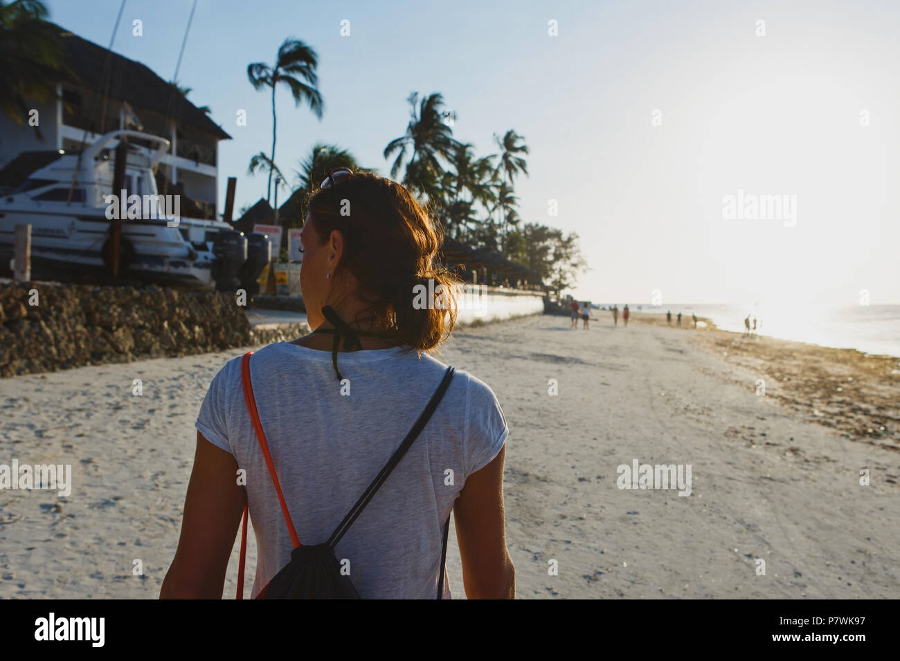 Ansicht von hinten junge Frau mit Rucksack zu Fuß entlang Ozean Küste bei Sonnenuntergang Stockfoto