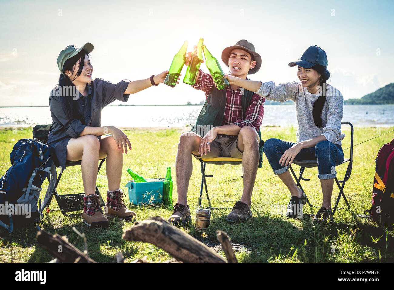 Genießen sie eine Gruppe von jungen asiatischen Freunde Picknick und Party am See mit Camping Rucksack und Stuhl. Junge Menschen Toasten und jubelnden Flaschen Bier. Mitarbeiter Stockfoto