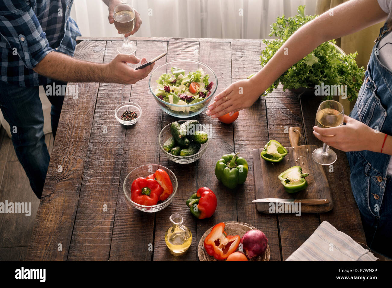 Mann nimmt Bilder von, wie seine Frau kocht das Abendessen Salat von Gemüse auf Holztisch in der Küche zu Hause Stockfoto