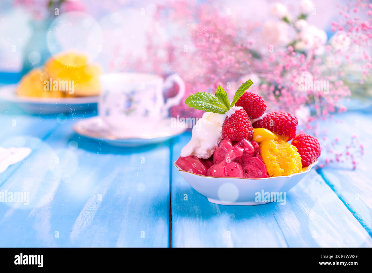 Obst Eis mit Himbeeren und Mango. Blumen und reife Mango auf einem blauen Hintergrund aus Holz. Frühstück ist süß und Kaffee. Stockfoto