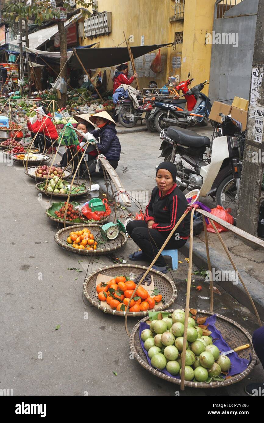 Auf einem Straßenmarkt im Freien in der Altstadt von Hanoi, Vietnam, stehen die Verkaufsverkäufer mit großen runden Obstkörben zum Verkauf Stockfoto