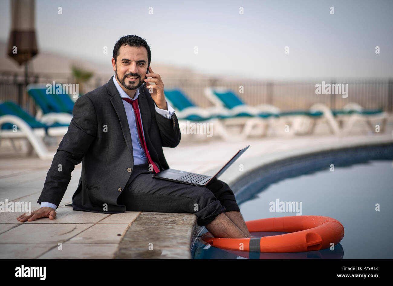 Im mittleren Alter arabischer Mann arbeiten während seinen Sommerurlaub durch einen Pool Stockfoto
