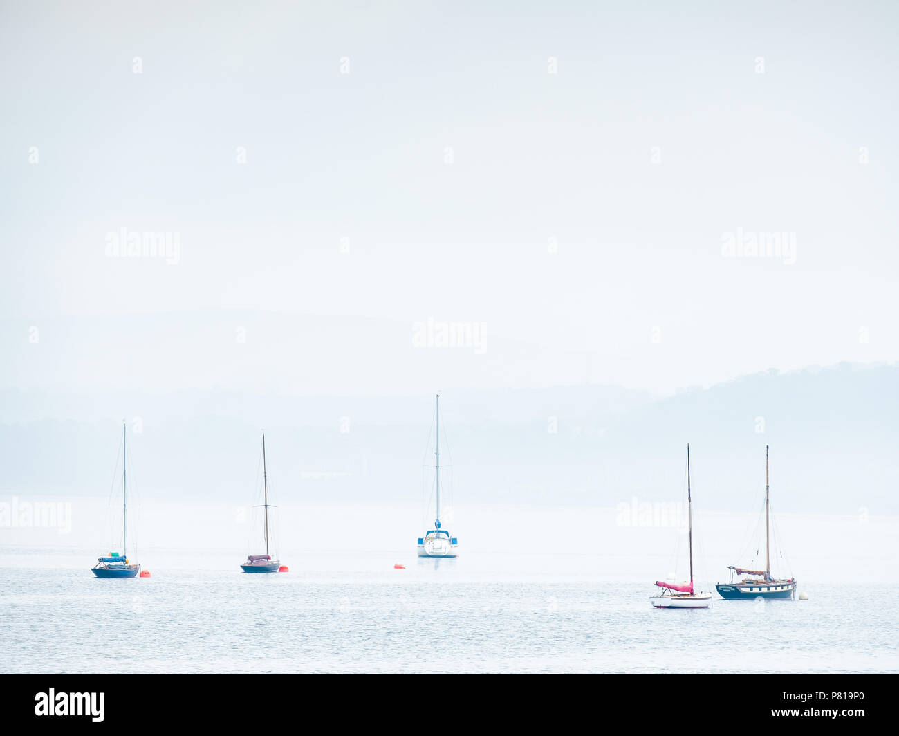 Fünf segeln Boote in Beaumaris auf der Insel Anglesey in Wales an einer ruhigen und sonnigen Tag mit Nebel rollen in Stockfoto