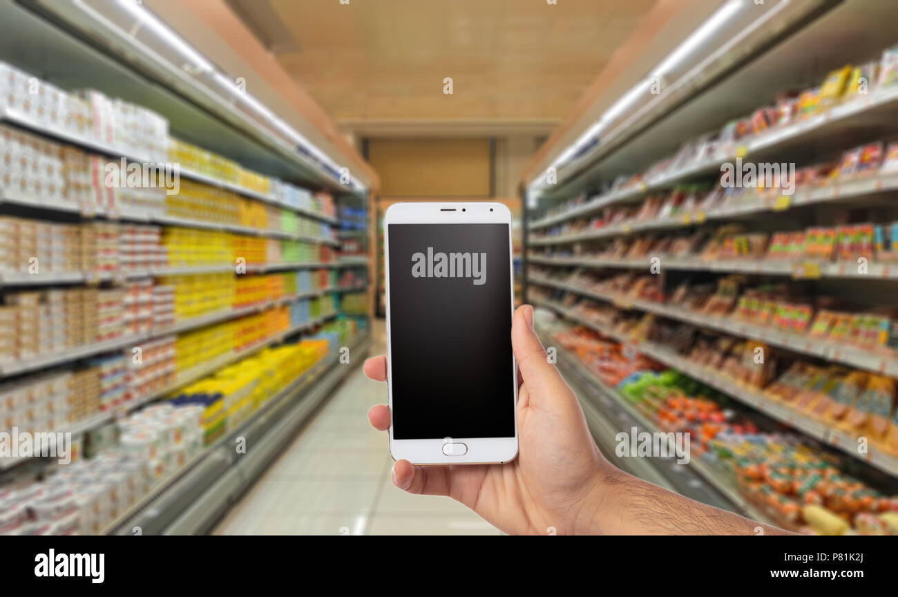Männliche Hand, die ein Smartphone mit leeren schwarzen Bildschirm auf Blur super Markt Hintergrund Kopie Raum Stockfoto