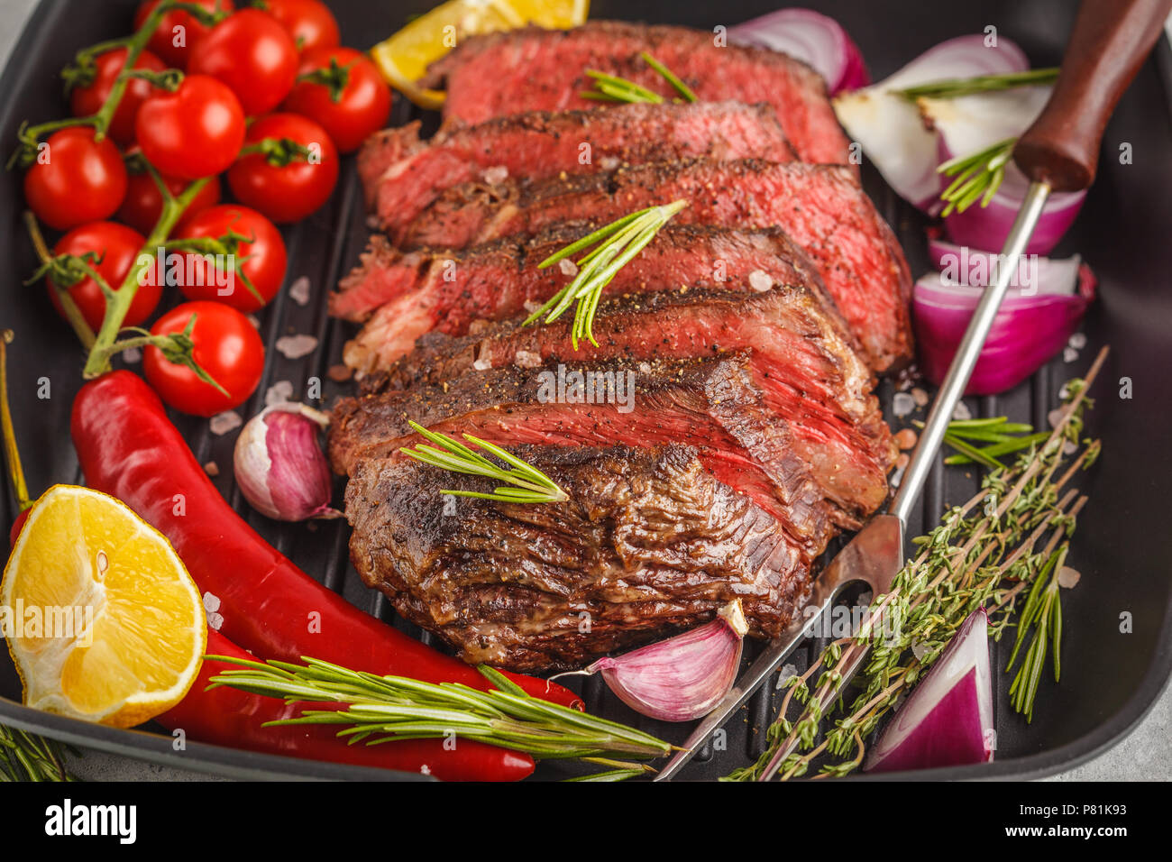 Roastbeef in Scheiben in einer Pfanne mit Gewürzen und Gemüse, dunklen Hintergrund. Stockfoto