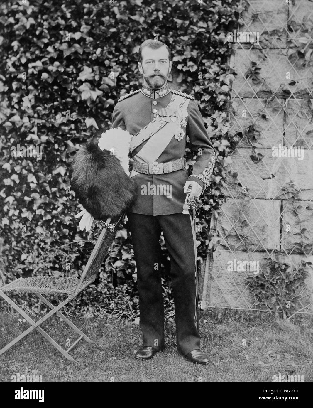 Englisch: Foto von Nikolaus II., Kaiser von Rußland, außerhalb Balmoral. Er trägt eine britische Uniform und hält eine Bärenfellmütze hat in seiner rechten Hand ein Schwert und in der linken. Es ist eine Mauer teilweise mit Efeu hinter ihm und ein Stuhl auf der linken Seite. 1896 Nikolaus II., seiner Gemahlin Alexandra Feodorowna und seine älteste Tochter Großfürstin Olga Nikolajewna besuchte Königin Victoria im Balmoral. Alexandra Feodorovna war eine Enkelin der Queen. 1896 287 Nikolaus II., Kaiser von Russland Stockfoto