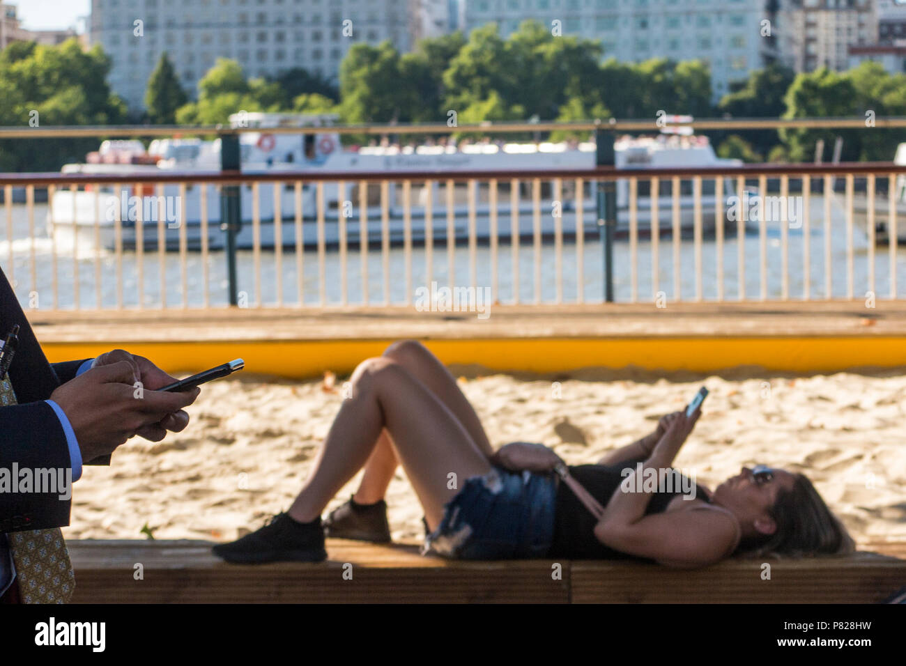 Ein Mädchen schaut sie auf dem Londoner Southbank, während ein Mann durch, auch auf seinem Smartphone suchen Smartphone Stockfoto